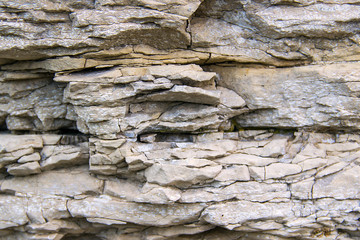 The texture of the stone wall of the rock with multi-colored shades, cracks, chips, scratches and small stones.