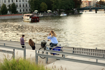 Dziewczyna, biznesmen jedzie na rowerze wzdłuż rzeki i rozmawia przez telefon. - obrazy, fototapety, plakaty