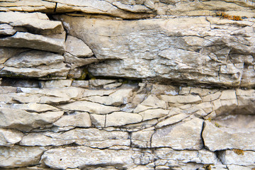 The texture of the stone wall of the rock with multi-colored shades, cracks, chips, scratches and small stones.