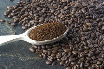 A grain of coffee and a wooden spoon with ground coffee on a dark background.
