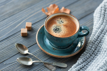 Blue cup whith coffee, knitted sweater, autumn leaves on wooden background. Cozy morning.