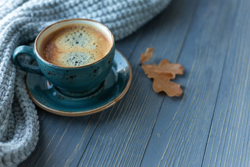Blue cup whith coffee, knitted sweater, autumn leaves on wooden background. Copy space.