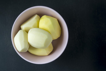 Peeled raw potatoes in a plate on a black background.