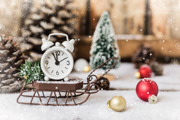 Christmas and New year alarm clock with snow on wooden sled with cones and toys, snowflakes texture