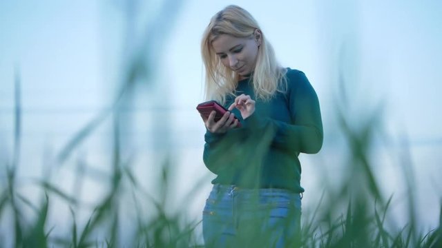Blond hair woman reads mobile phone news and messages at the natures with blue sky