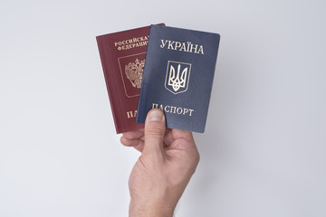 Ukrainian and Russian international passports in the man's hand. White background. Close up