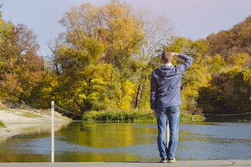 Fototapeta na wymiar Man with arms raised standing on the dock. Autumn, sunny. Back view