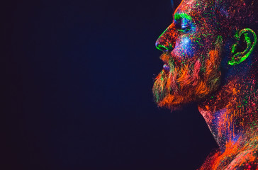 Concept. Portrait of a bearded man. The man is painted in ultraviolet powder.