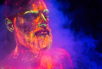 Bearded man painted in fluorescent powder on a background of smoke.