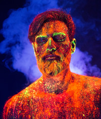 Bearded man painted in fluorescent powder on a background of smoke.