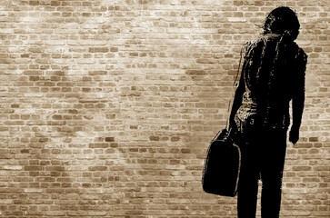 Graffiti/shadow on a brickwall showing a refugee girl walking with her suitcase