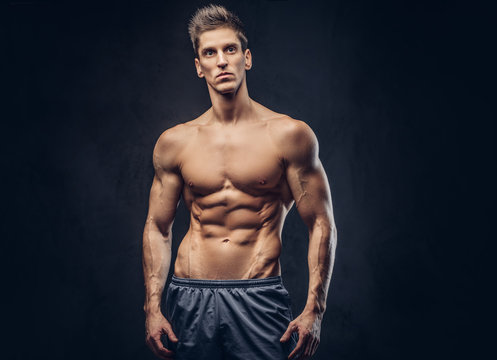 Handsome shirtless ectomorph bodybuilder with stylish hair posing on a dark background.