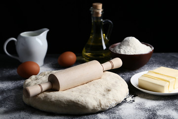 Raw dough with rolling pin, butter in plate and eggs on wooden table