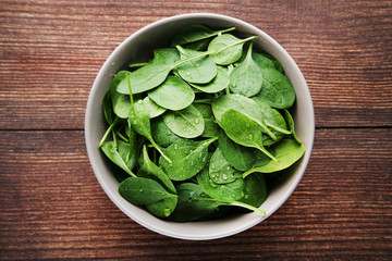 Spinach leafs in bowl on brown wooden table