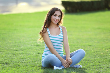 Fototapeta na wymiar Young woman sitting on green grass in the park