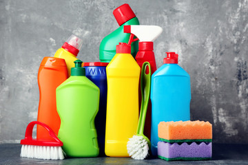 Bottles with detergent and cleaning tools on grey background