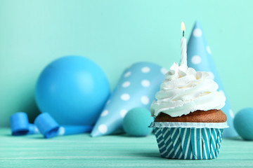 Cupcake with candle, paper cap and balloon on mint background
