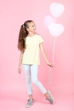 Cute young girl with balloons on pink background