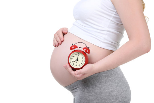 Pregnant woman holding alarm clock on white background