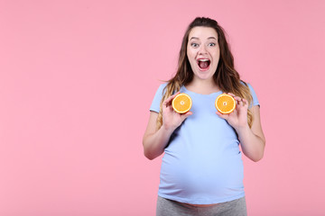 Beautiful pregnant woman with orange fruit on pink background