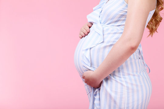 Pregnant woman in striped dress on pink background