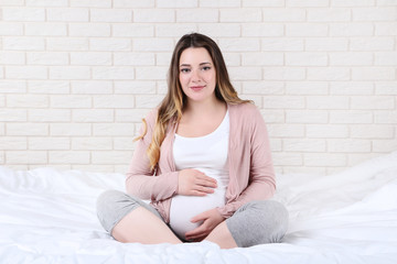 Beautiful pregnant woman sitting on bed