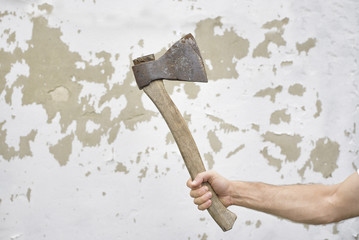 Old rusty ax in the man's hand against the shabby wall.