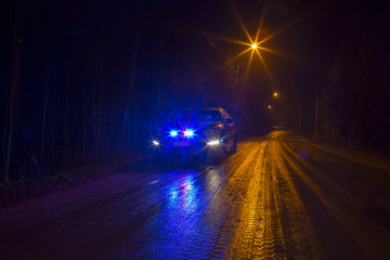 Police car on a dark and wet road flashing blue and red light. Rainy and dark weather. Image has a...