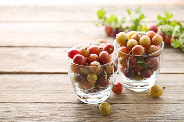 Ripe gooseberries fruit in glass on grey wooden table