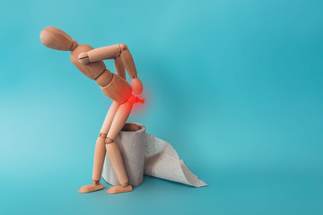 Wooden figure sit on a roll of toilet paper. Concept of the problem with hemorrhoids. - obrazy, fototapety, plakaty