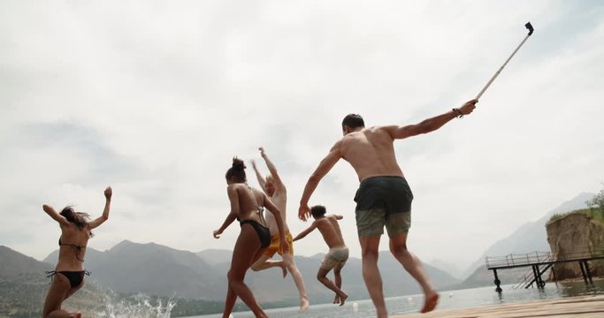 Group of young friends jumping from pier into lake, enjoying their holiday, having fun 4k
