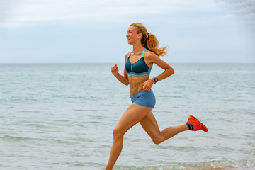 Beautiful sportive woman running along beautiful sandy beach, healthy lifestyle, enjoying active summer vacation near the sea