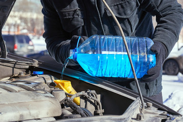 Man filling a windshield washer tank of a car on a street in winter day
