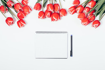Blank notepad and pen under blooming red flowers