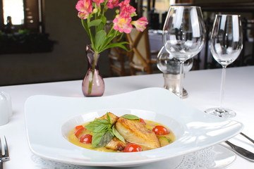fried fish in sauce with cherry tomatoes and basil on white background