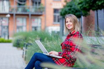 Portrait of a young beautiful girl with notebook computer sitting at bench near a house.