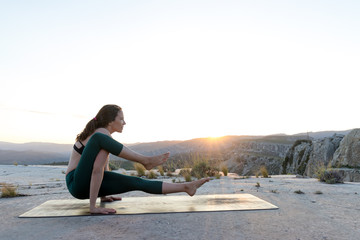 Woman practicing yoga on mountain top during sunset