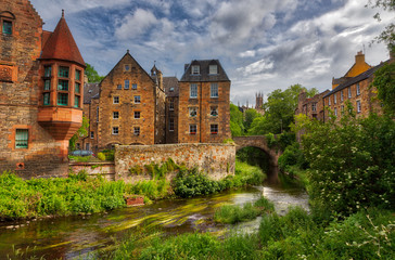 Fototapeta na wymiar Quaint stream with green flora along it flowing through Dean Village in Edinburgh with old Scottish buildings