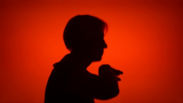 Silhouette of happy senior woman dancing silly on red background. Female's face in profile having fun. Black contur shadow of grandmother's half-face fooling around