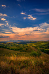 Naklejka na ściany i meble Beautiful view over the picturesque hills with a sky full with beautiful clouds at sunset