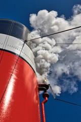 Closeup of a steamboat whistle blowing out white steam from the stack and a clear blue sky in the...