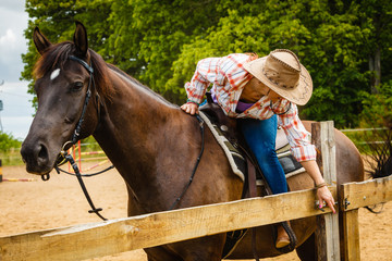 Cowgirl getting horse ready for ride on countryside