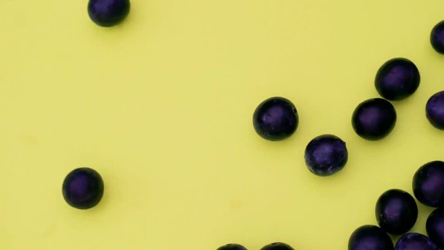 Runde frische reife Pflaumen rollen in das Standbild. Sie bedecken einen gelben Hintergrund, der f&uuml;r chroma keying geeignet ist. Aufnahme in Echtzeit von oben.