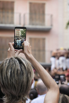 Woman holding a mobile phone taking a photo of human towers in Catalonia during travel. Empty cooy space for Editor's text. 