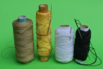 a row of bobbins with colored threads and needles on a green table