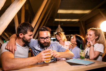 Two brutal men clinking glasses of beer in a cafe sitting at the table