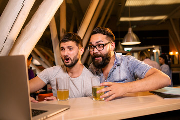 Two men watching the broadcast of a sports match sitting with a beer at the table in the tavern