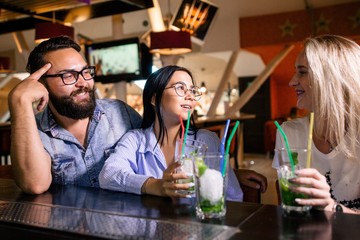 Three cheerful friends with alcoholic drinks sit at the bar in the tavern