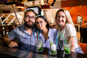 Three cheerful friends sit at the bar looking at the camera