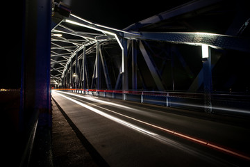 Old vintage (rail) bridge over the river 'IJssel' with industrial character. Exposure lights of passing cars and trains.